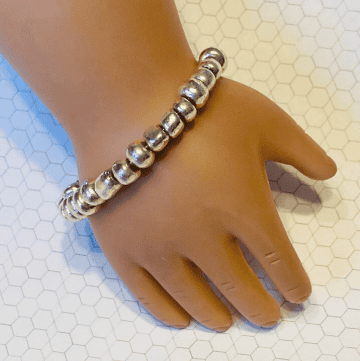 18 inch doll hand with a silver bead bracelet on it's wrist.