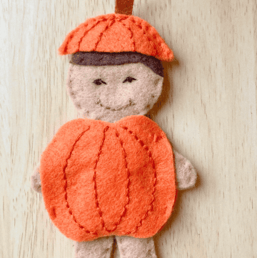 felt doll child wearing and orange pumpkin around his body and a pumpkin stem hat