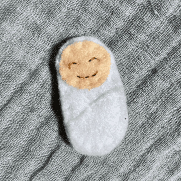 felt doll baby in a white bundle on a blue blanket background