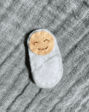 felt doll baby in a white bundle on a blue blanket background